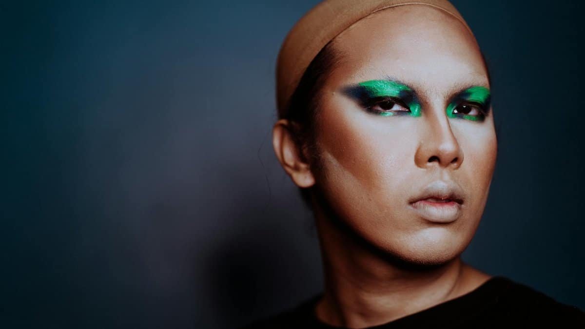 A striking portrait of an individual with bold, colorful makeup and a neutral expression.
