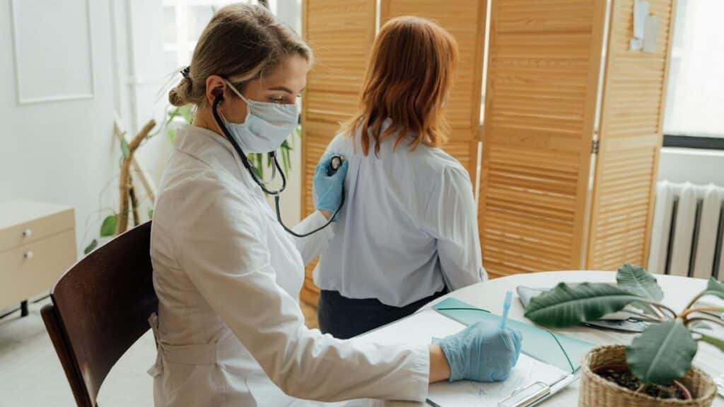 Female doctor examining a patient with a stethoscope in a medical office.