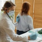 Female doctor examining a patient with a stethoscope in a medical office.