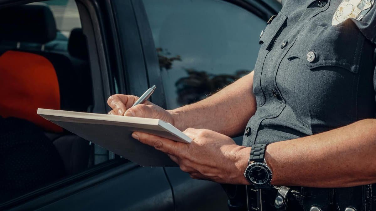 Close-up of a police officer writing a ticket by a car window. Law enforcement scene.