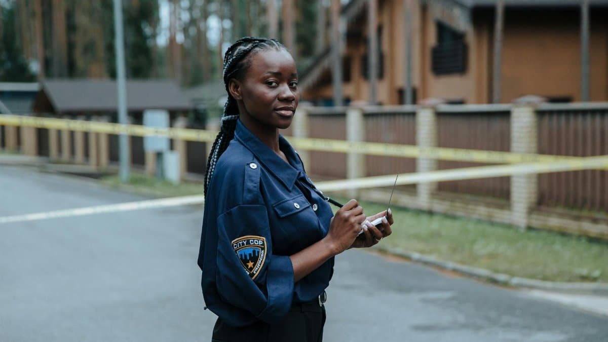 A female police officer standing outdoors near caution tape and concrete buildings during the day.