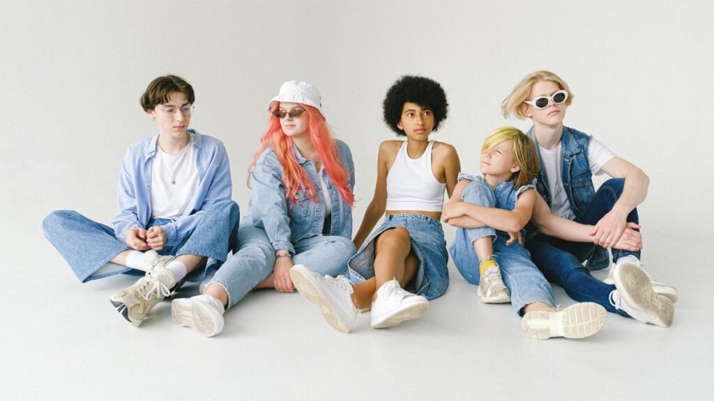 Full body of serious multiracial teens and small girl wearing denim outfits sitting on floor against white wall