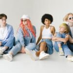 Full body of serious multiracial teens and small girl wearing denim outfits sitting on floor against white wall