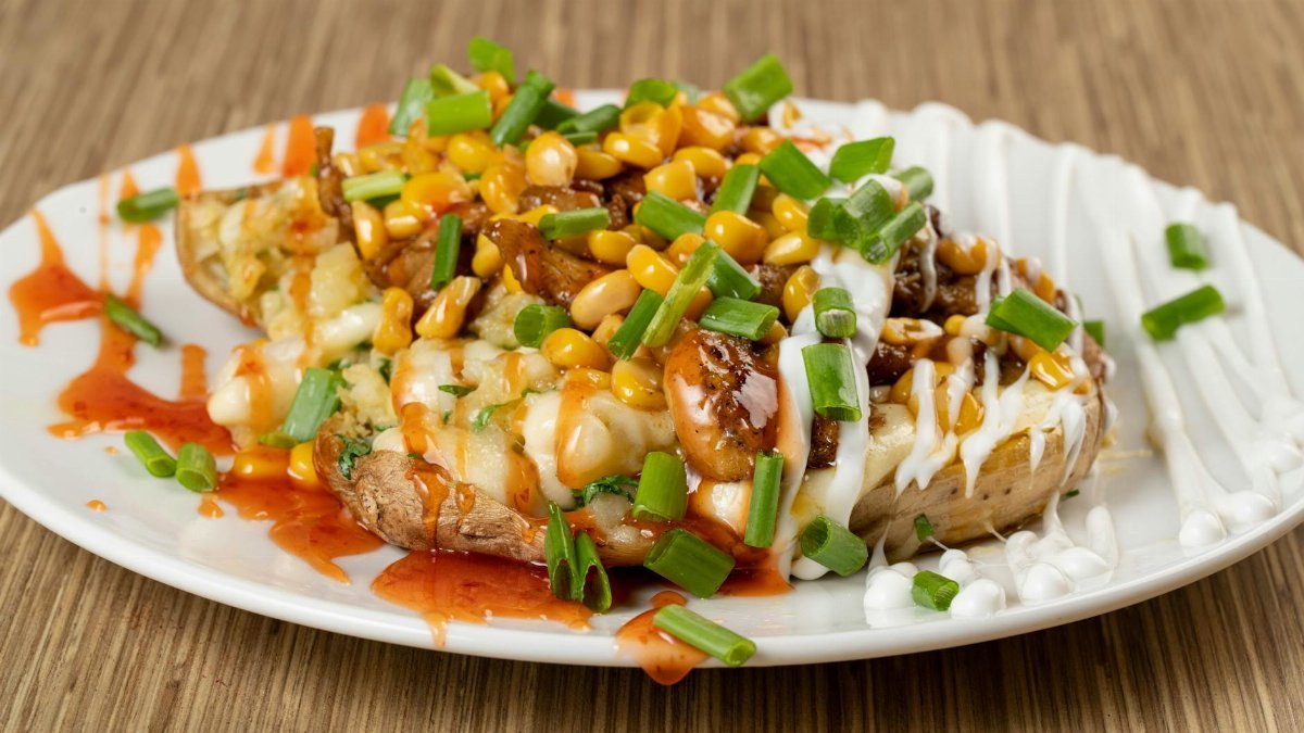 Delicious loaded baked potato with cheese, corn, and chives, drizzled with sauces.