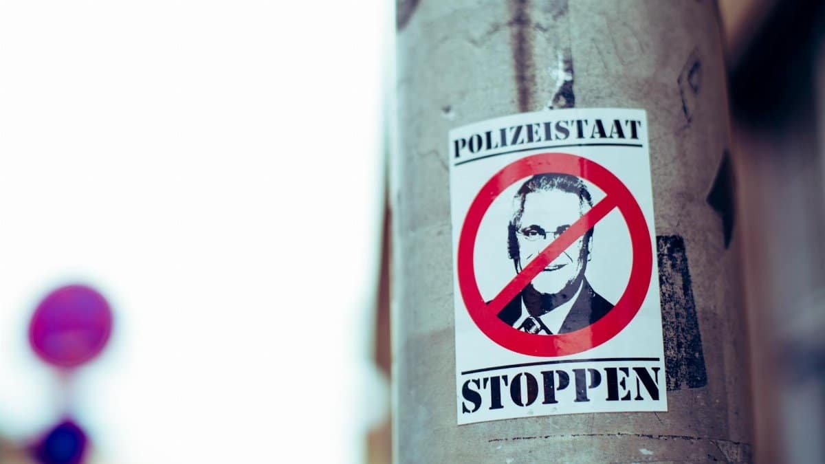 Close-up of a political protest sticker on an urban concrete post, featuring anti-establishment imagery.