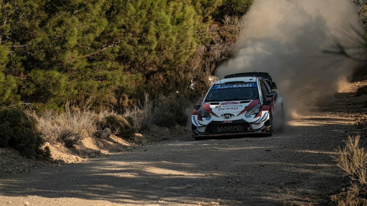 A rally car races through a dusty forest track, kicking up dust, capturing the thrill of motorsport.