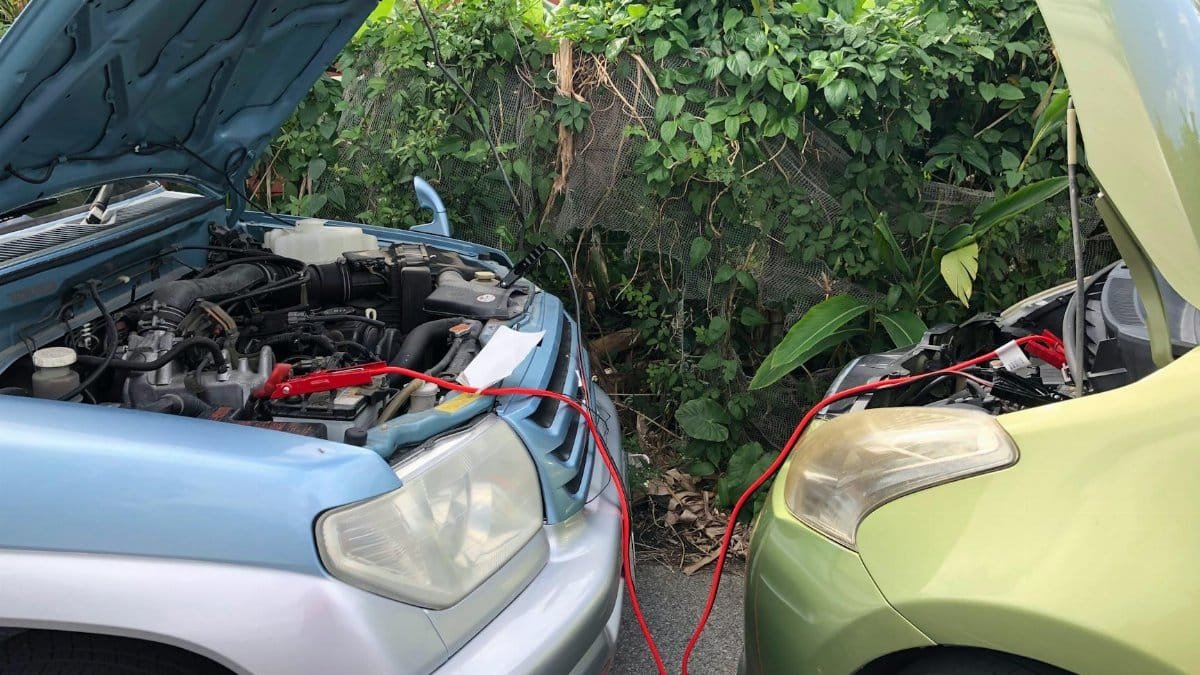 Two cars connected by jumper cables in a parking lot for a battery charge.