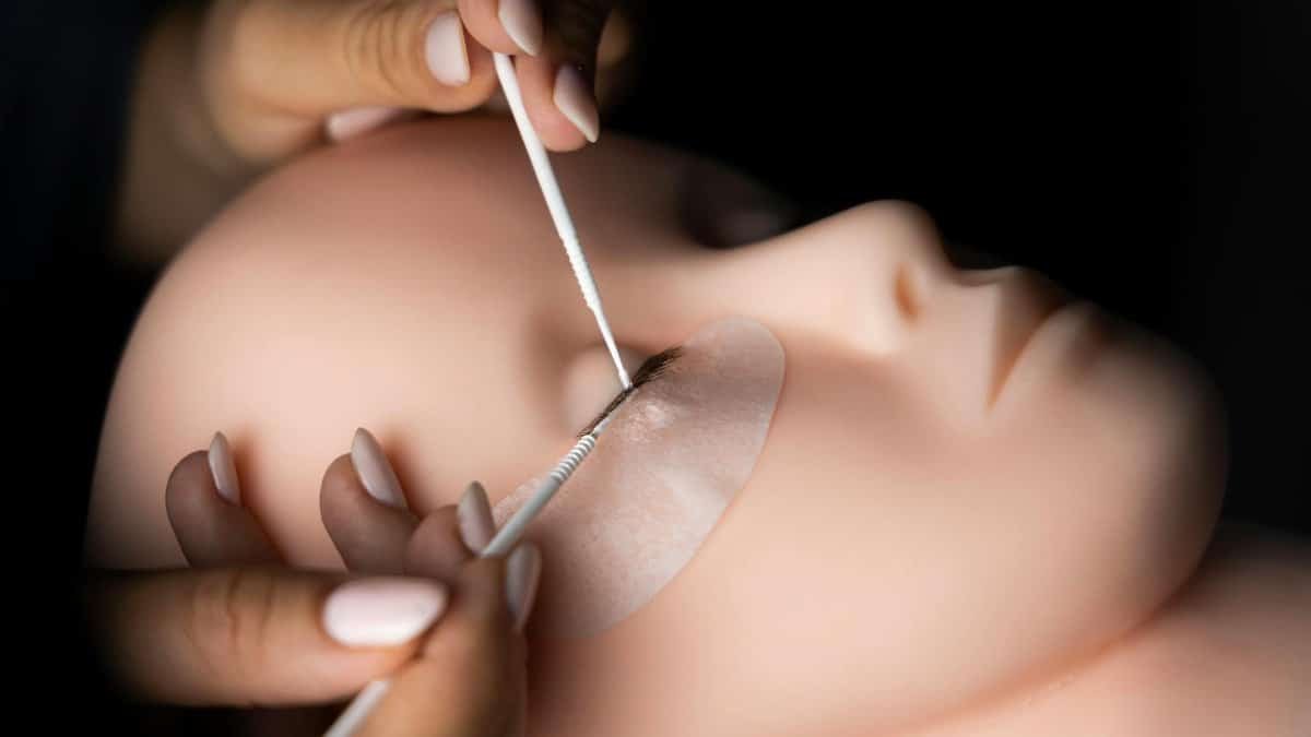 Close-up of a beautician practicing eyelash extensions on a mannequin head with precision and focus.
