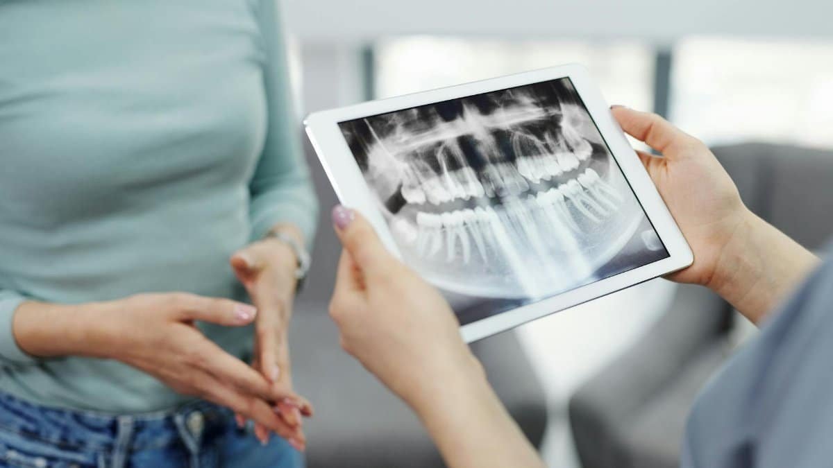 A dentist displays a dental x-ray on a tablet to a patient during a consultation.