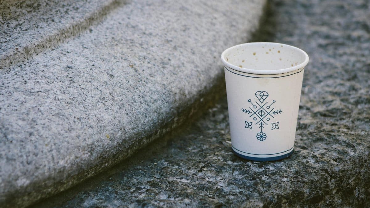 A disposable coffee cup with decorative design placed on outdoor stone steps.