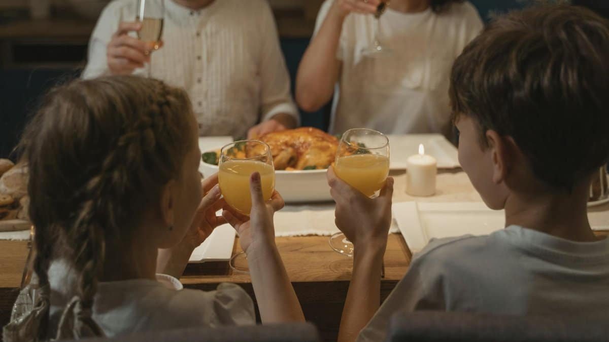Two children and adults together at a cozy family dinner table, raising glasses in a toast.