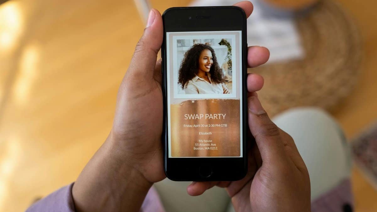 Close-up of hands holding a smartphone displaying a swap party invitation on the screen.