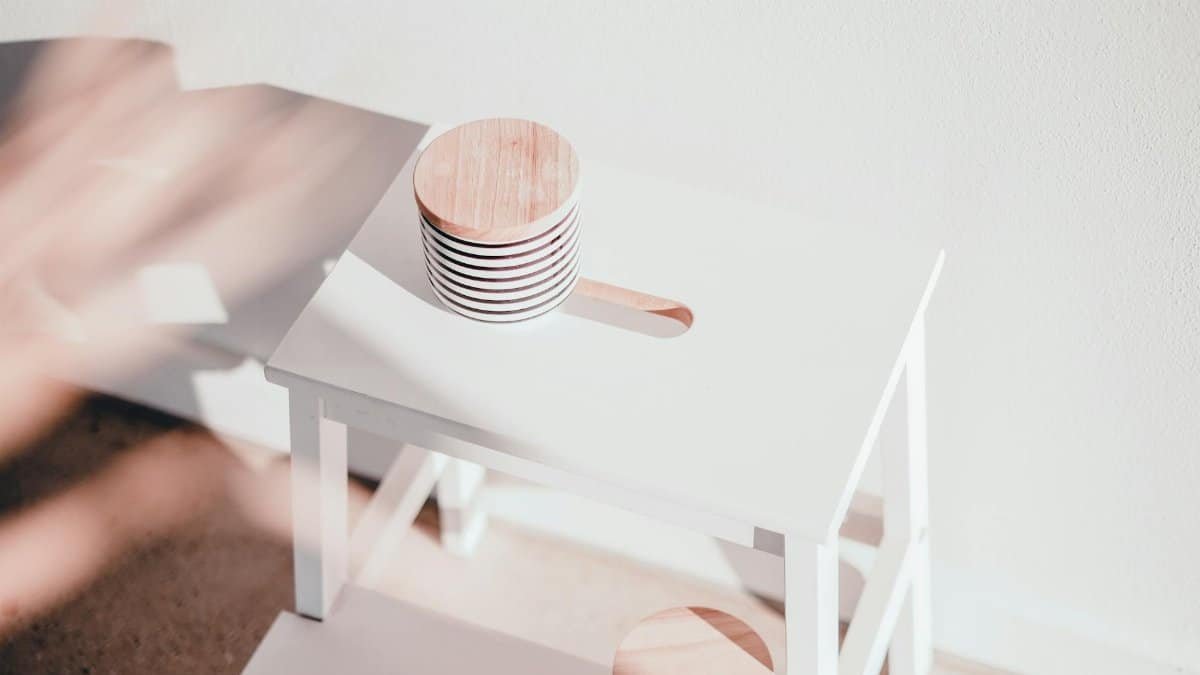 A white wooden step stool with circular toppers bathed in natural sunlight, casting shadows.
