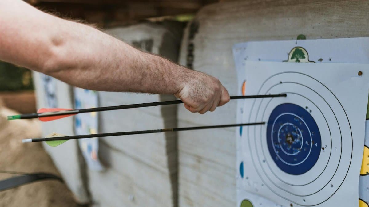 A focused arm holding arrows near a target in an archery practice setting.