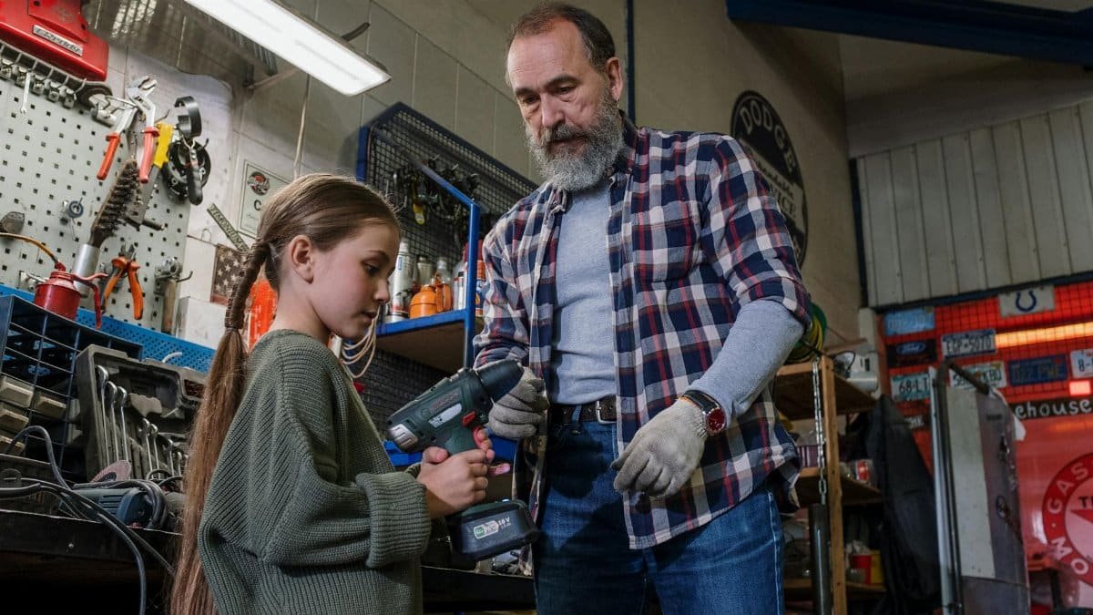 Father and daughter share bonding time in an auto workshop, using power tools.