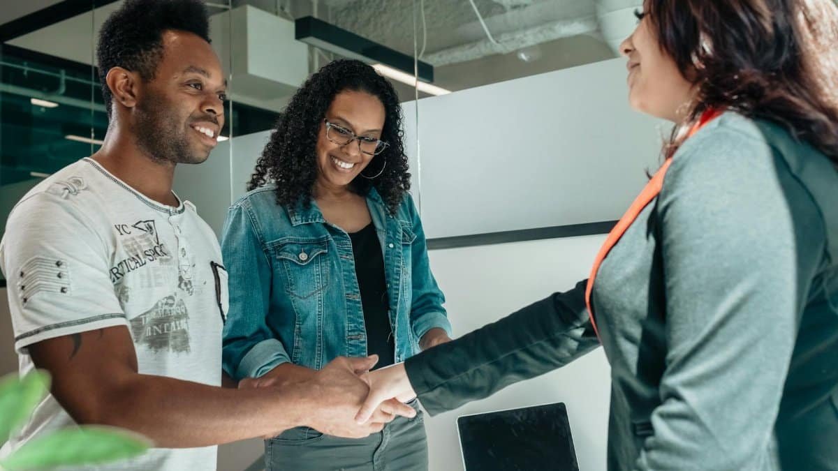 Smiling couple shaking hands with advisor in modern office.