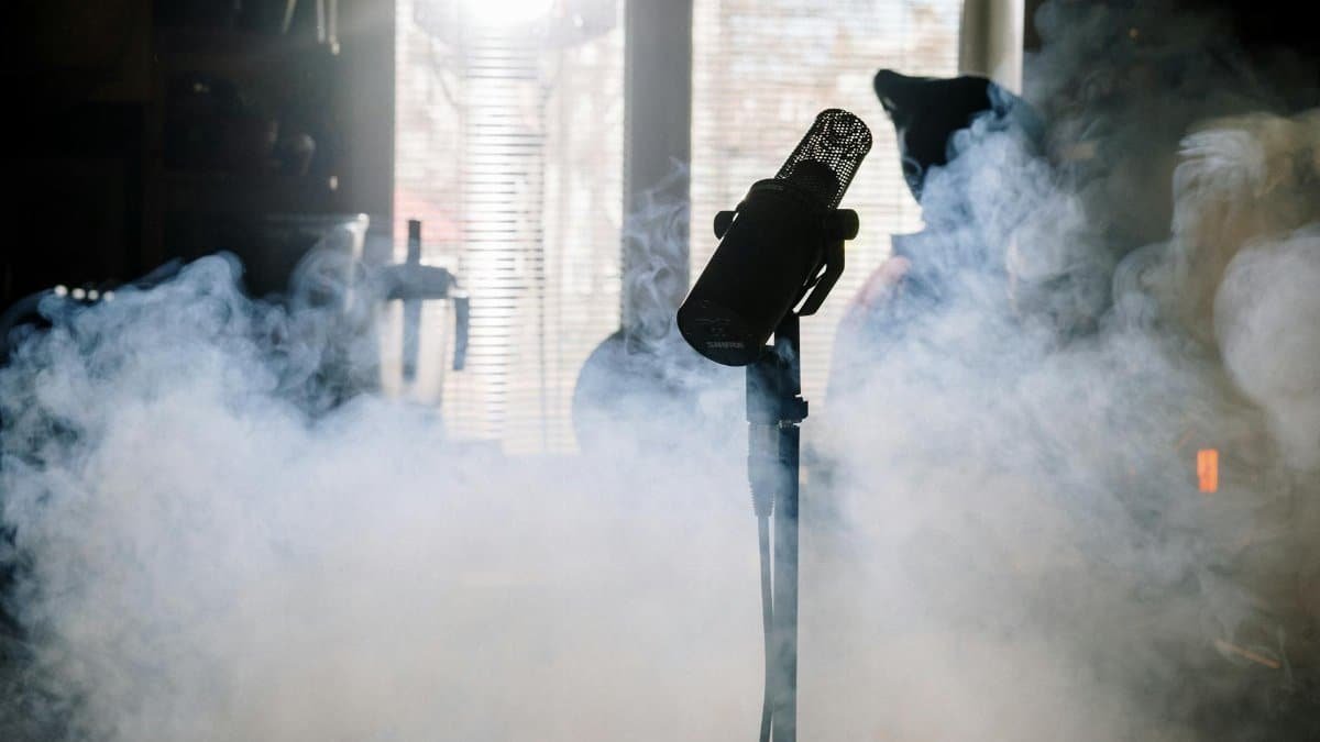 A mysterious microphone stands amidst swirling smoke in a sunlit home studio.