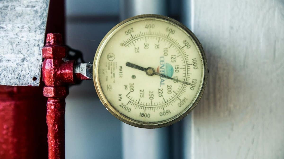 Detailed view of a pressure gauge attached to a red industrial pipe, measuring PSI and kPa.