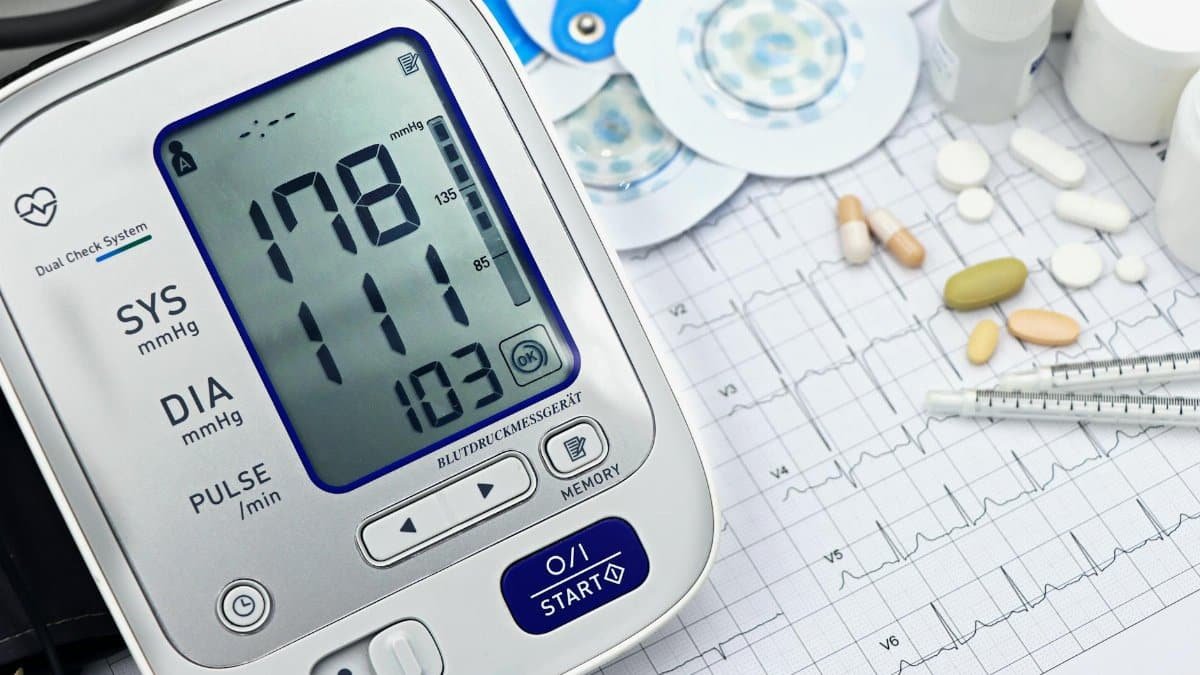 Close-up of a digital blood pressure monitor with ECG printout, pills, and medical tools.