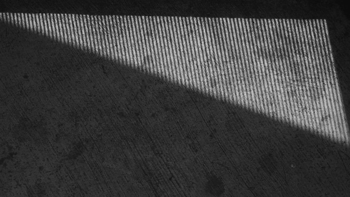 A high-angle view of light and shadow casting a pattern on a textured concrete floor.