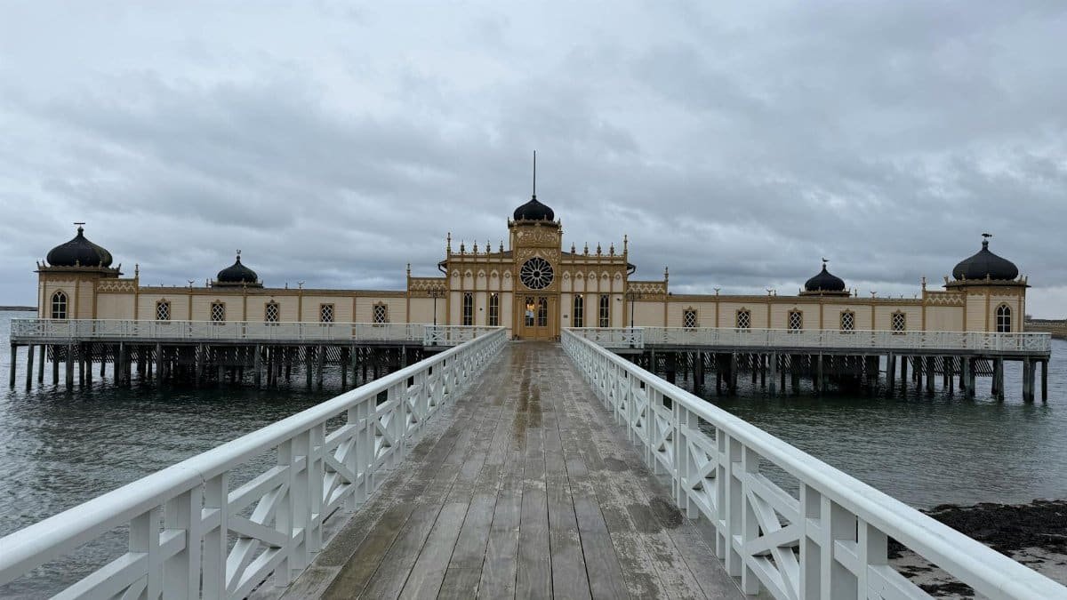 Symmetrical view of a historic bathhouse on a pier under a cloudy sky.