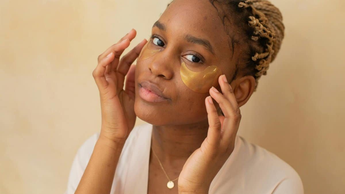Portrait of an African American woman applying under-eye patches indoors.