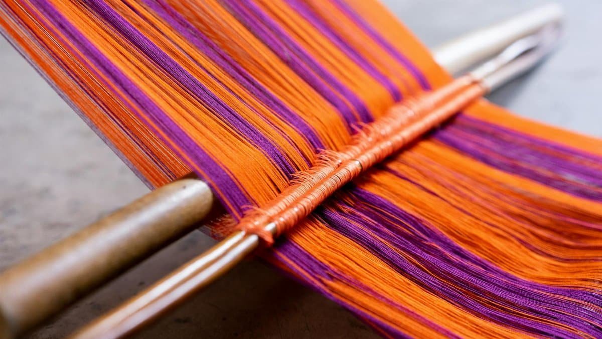 Detailed view of traditional weaving with bright orange and purple threads on a loom.