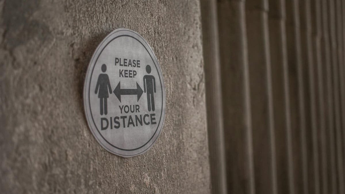 Circular sign on concrete wall promoting social distancing during pandemic.