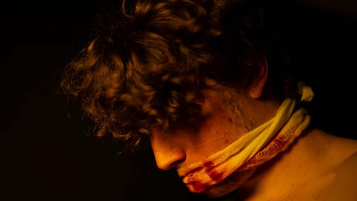 A dramatic portrait of a man with curly hair and gagged mouth under moody lighting, conveying strong emotions.