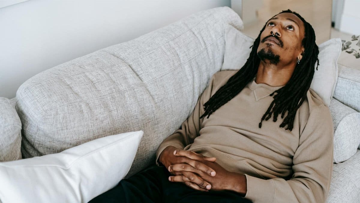Man with dreadlocks lies on couch, looking up, expressing contemplation and introspection indoors.