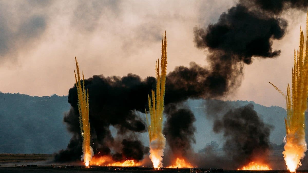 Intense scene of fire eruptions and smoke plumes rising against a cloudy sky, creating a dramatic atmosphere.