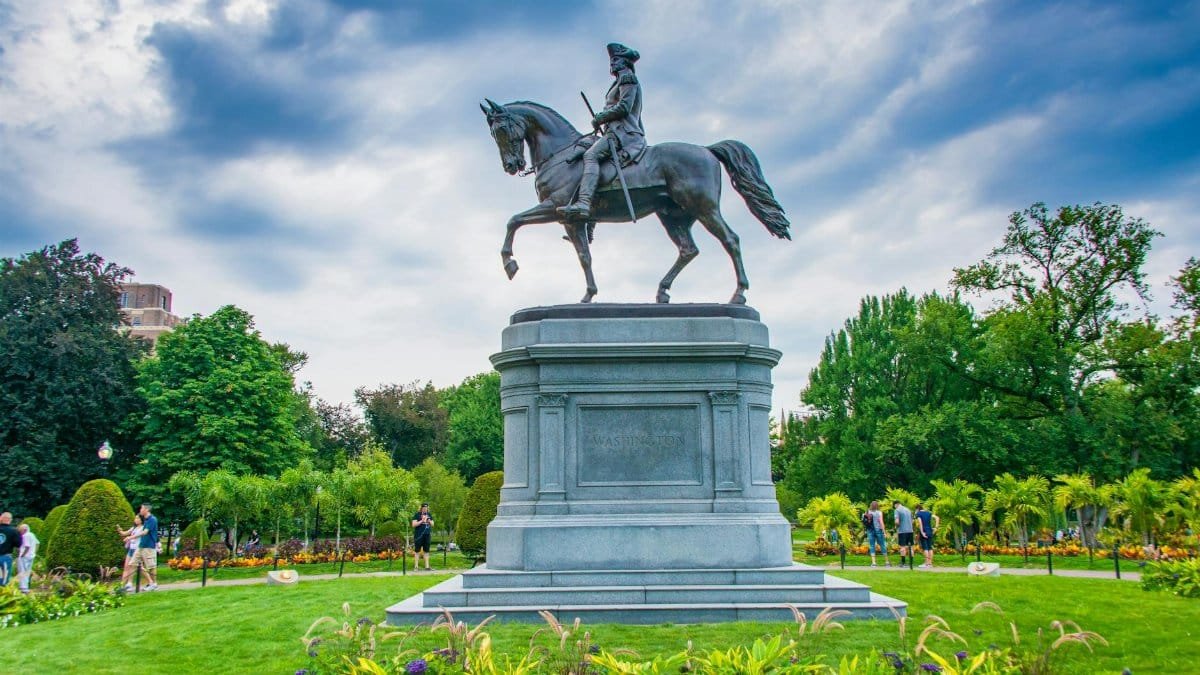Statue of George Washington on horseback in Boston Public Garden surrounded by foliage.