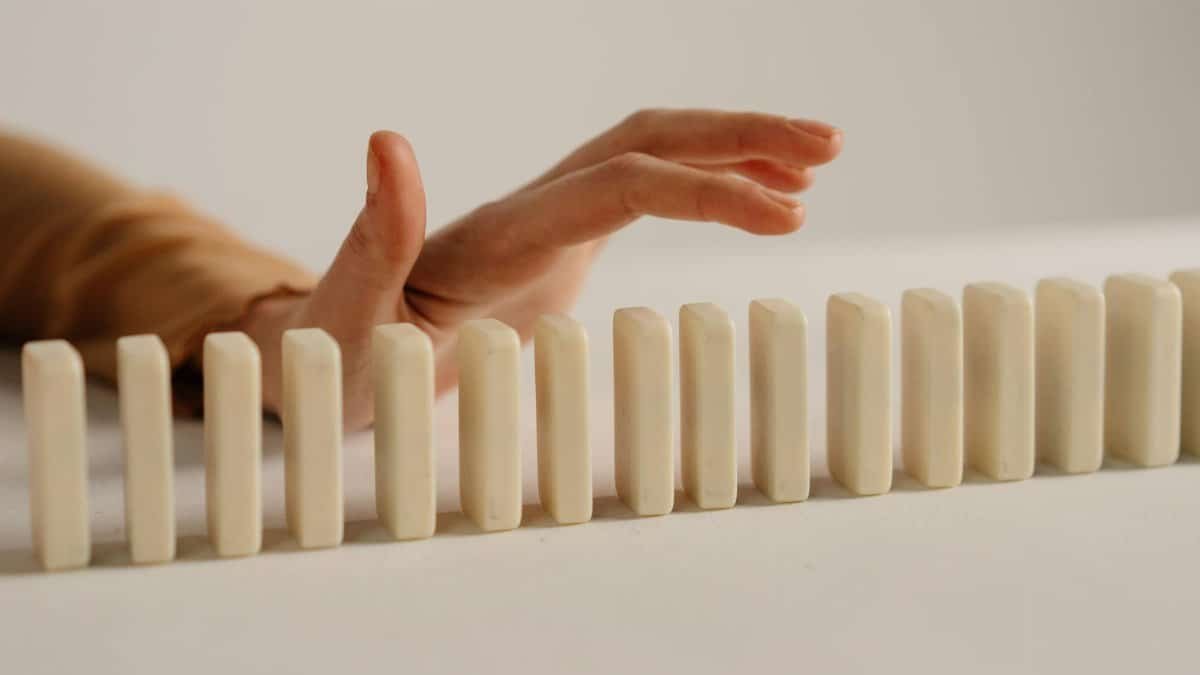 A hand poised to stop falling dominoes, depicting control and intervention.