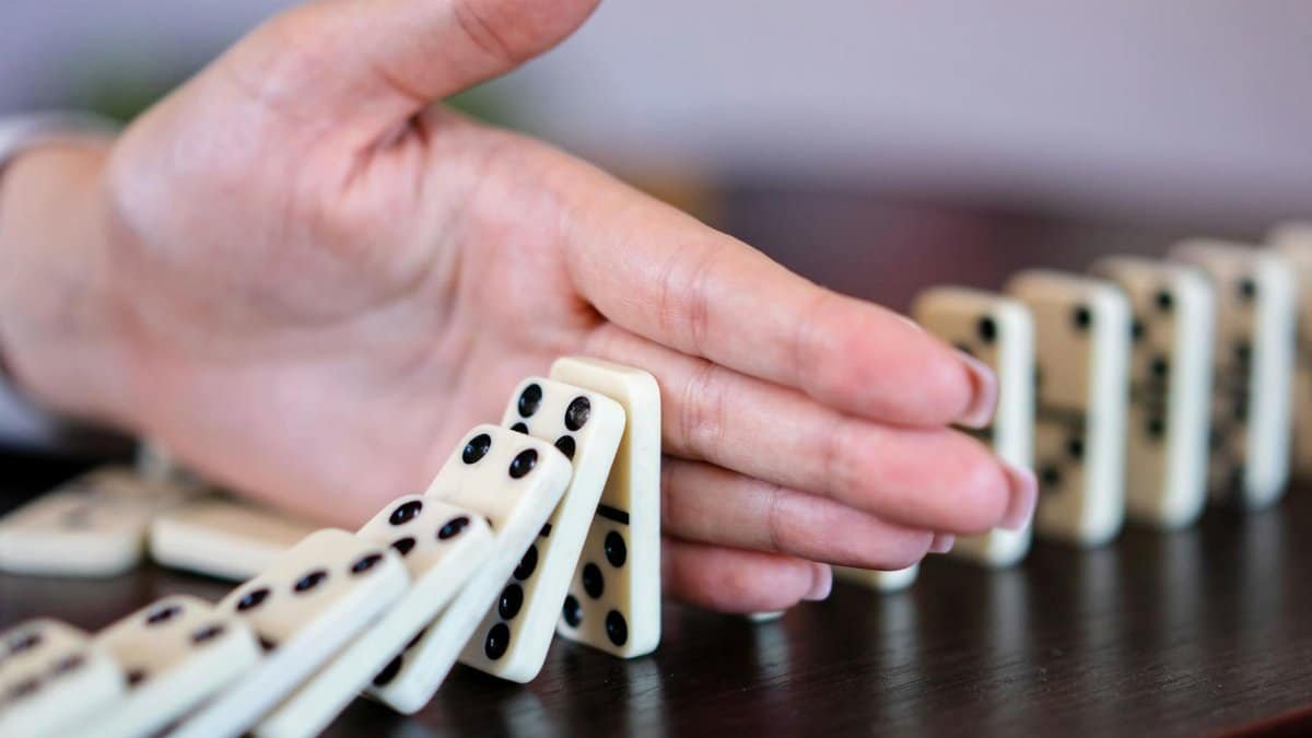 A close-up of a hand stopping a row of falling dominoes to illustrate strategy and control.