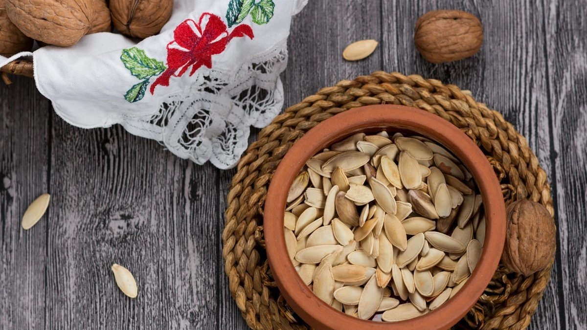 Close-up of pumpkin seeds in a terracotta bowl with walnuts on a rustic wooden surface. Perfect for food photography.