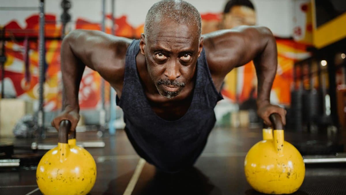 Strong senior adult engaged in kettlebell push-ups, demonstrating strength and focus indoors.