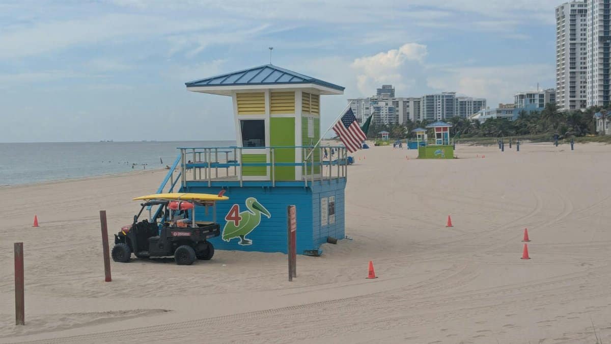 A vibrant lifeguard tower on Pompano Beach, Florida with a clear view of the ocean and nearby buildings in the background.