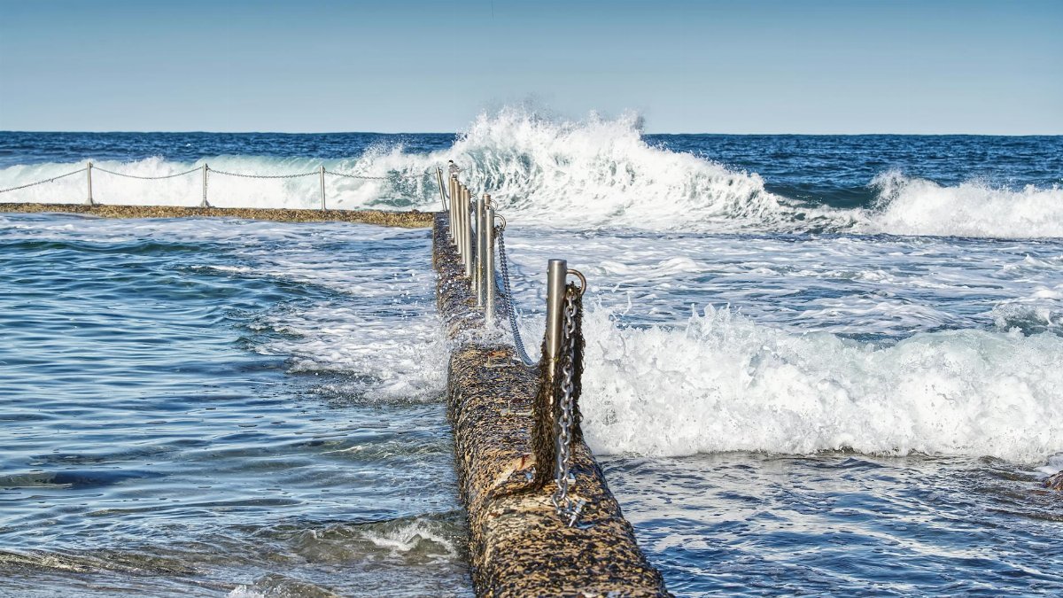 Dramatic ocean scene with waves crashing over a swimming pool barrier. Perfect for coastal themes.