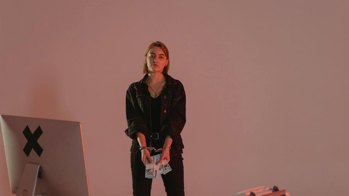A young woman in handcuffs holding cash amidst a digital crime setup.