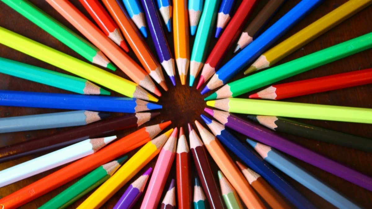 Vibrant spiral of colored pencils forming a rainbow spectrum on a wooden desk.