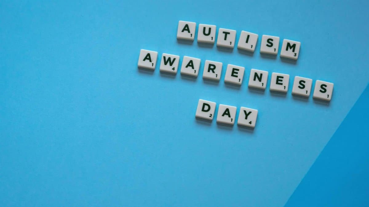 Scrabble tiles spelling 'Autism Awareness Day' on a blue background, highlighting awareness.