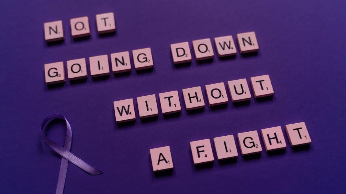 An inspirational quote made from Scrabble tiles alongside a purple awareness ribbon.