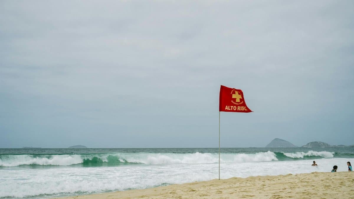 High-risk warning flag on a sandy beach with ocean waves and distant islands.