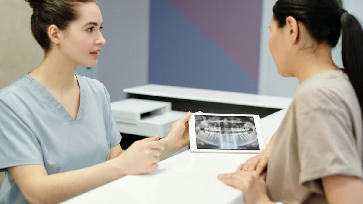 A dentist explains X-ray results to a patient using a tablet in a modern dental clinic.
