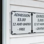 Bilingual sign displaying admission prices in English and French at building entrance.