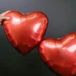 Two hands holding heart-shaped balloons against a black background, symbolizing love and romance.