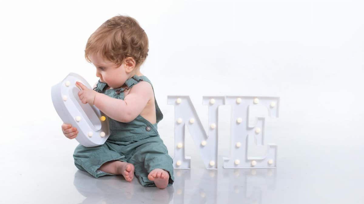 Cute baby sitting with illuminated 'One' sign, celebrating first birthday. Perfect for milestone moments.