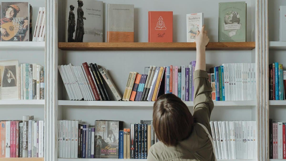 An individual browsing a bookshelf and reaching for a book in a bookstore setting.