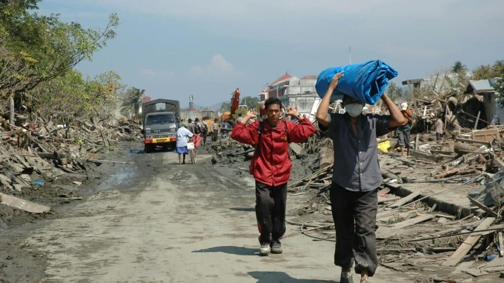 People walking through debris in Banda Aceh after a natural disaster, reflecting resilience.