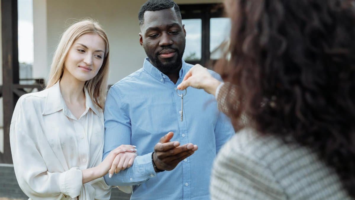 Happy couple receiving keys to their new home from real estate agent outdoors.